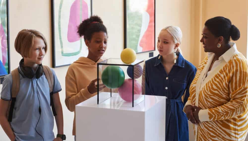 Students and a teacher examining a colorful sculpture exhibit during a museum gallery tour
