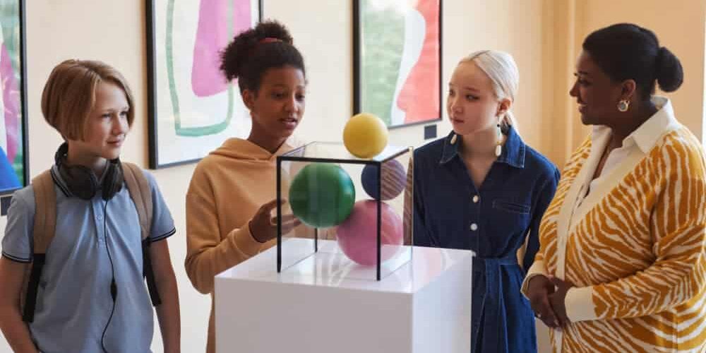Students and a teacher examining a colorful sculpture exhibit during a museum gallery tour